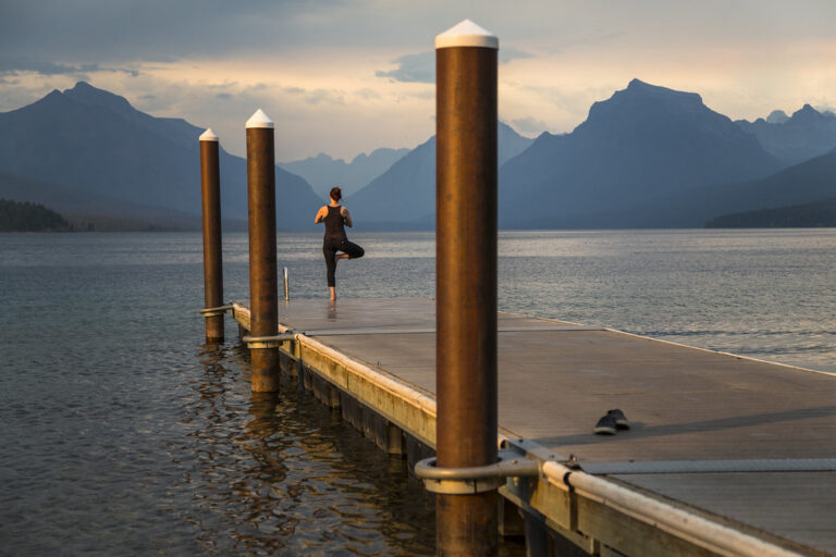 Person holding a tree yoga pose on a wooden dock by a calm mountain lake