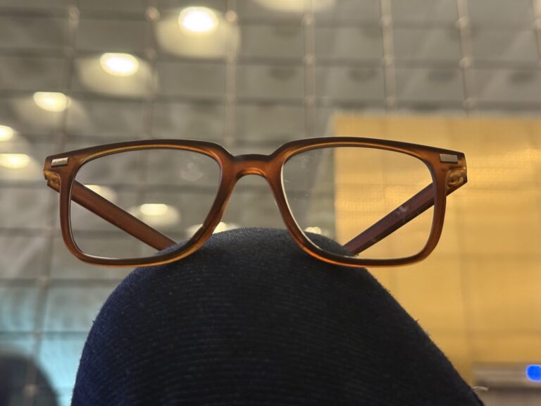 Brown eyeglasses resting on a person's knee in a softly lit room