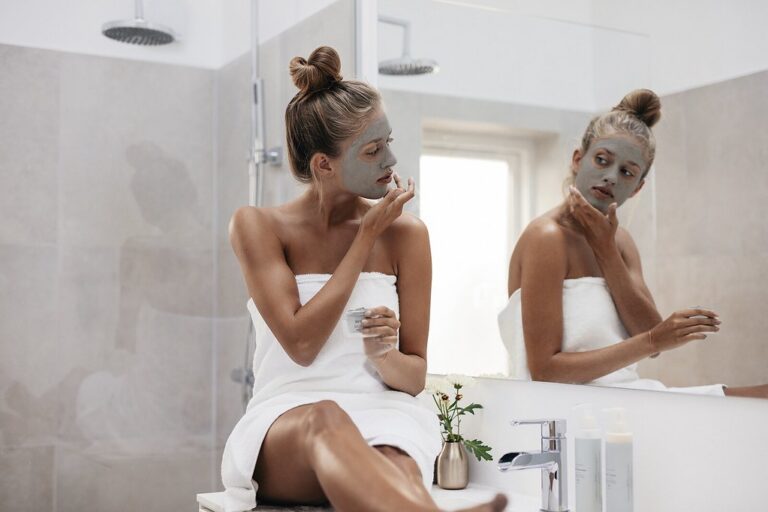 Two women in white towels applying face masks in a bright bathroom