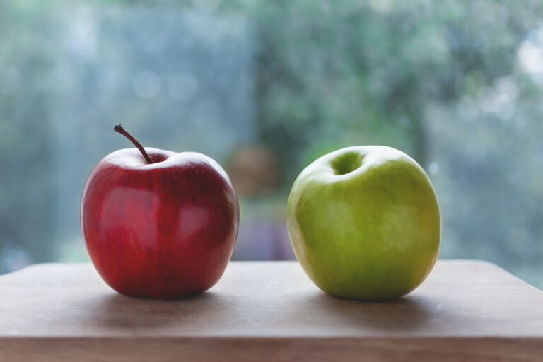 A shiny red apple and a green apple side by side on a wooden table
