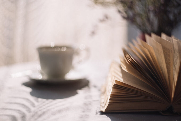 White cup of tea beside an open book on a bright table