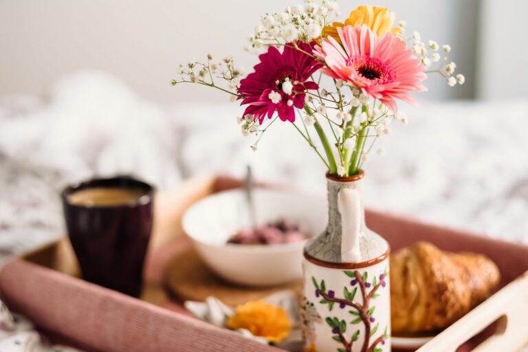 Breakfast tray in bed with coffee, a croissant and a vase of bright flowers