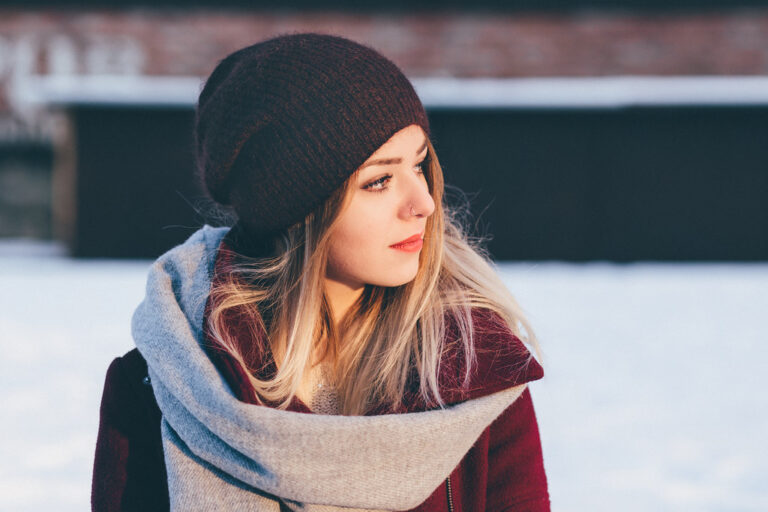 Young woman in a knit hat and soft scarf standing outdoors on a snowy winter day