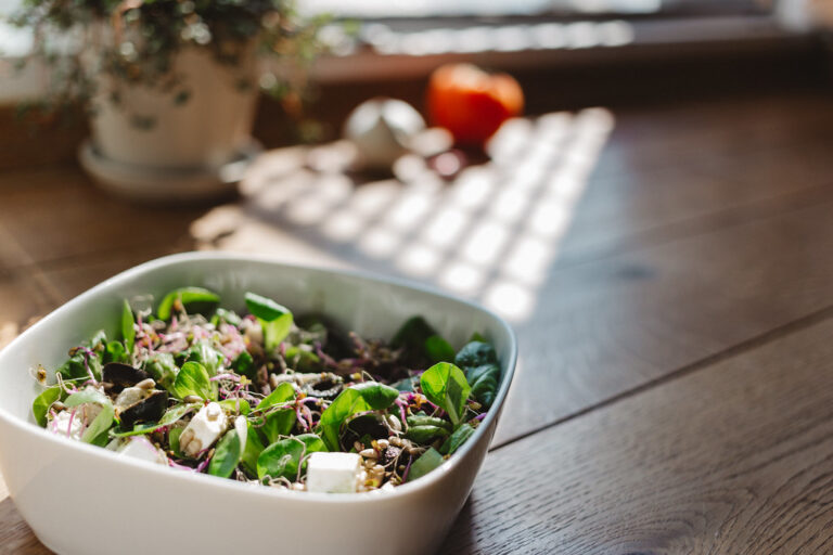 Fresh green salad in a white bowl on a sunny wooden kitchen table