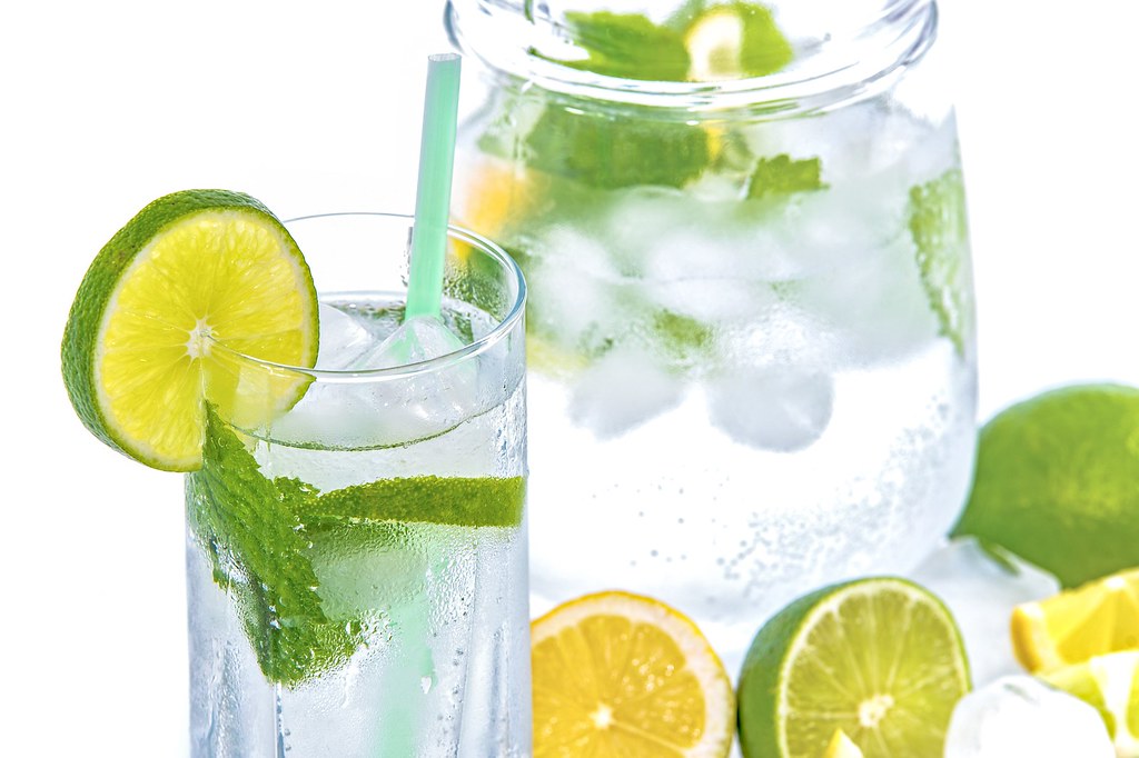 Glass of sparkling water with lime slices and fresh mint beside a water jug