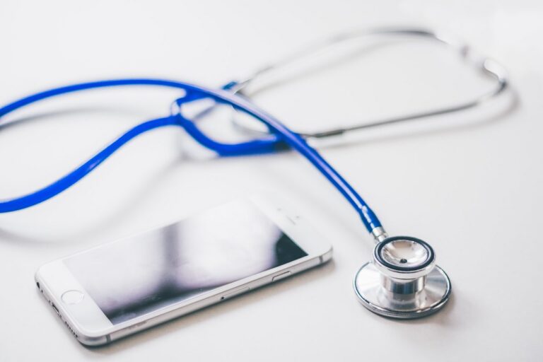Blue stethoscope resting beside a smartphone on a clean white surface
