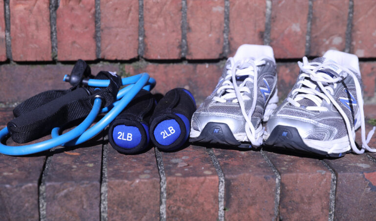 Running shoes, light hand weights and a blue resistance band resting on a brick step