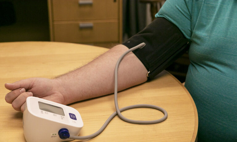 Person checking blood pressure at home with an arm cuff monitor resting on a table