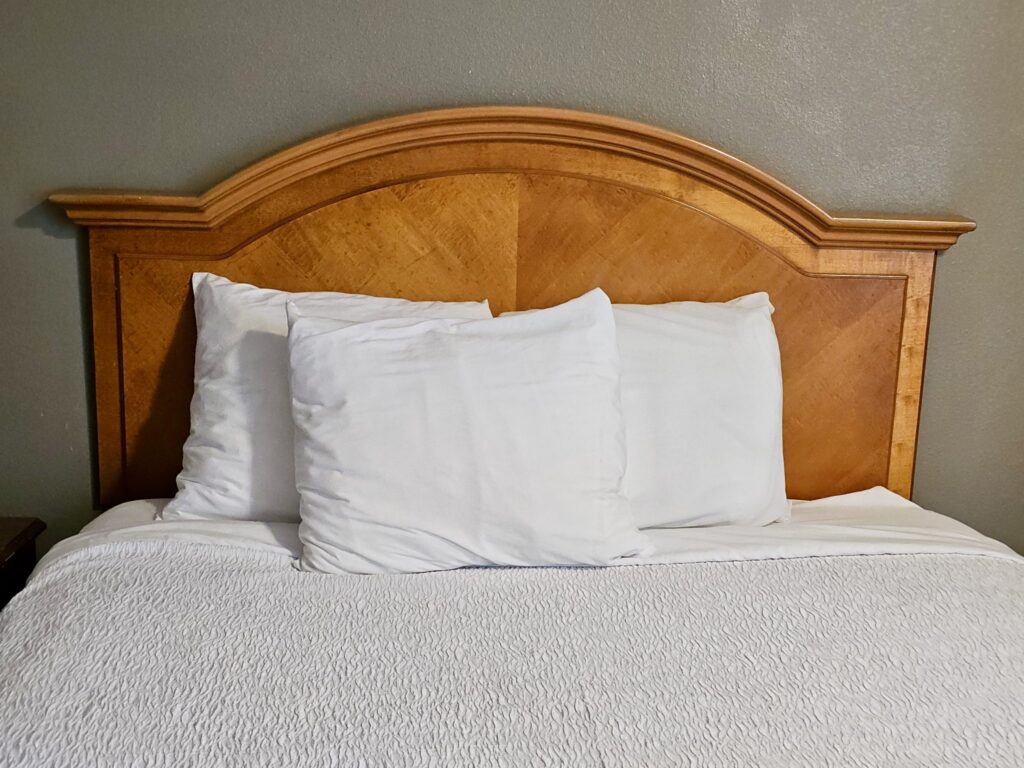 Neatly made bed with white pillows and white bedding against a wooden headboard