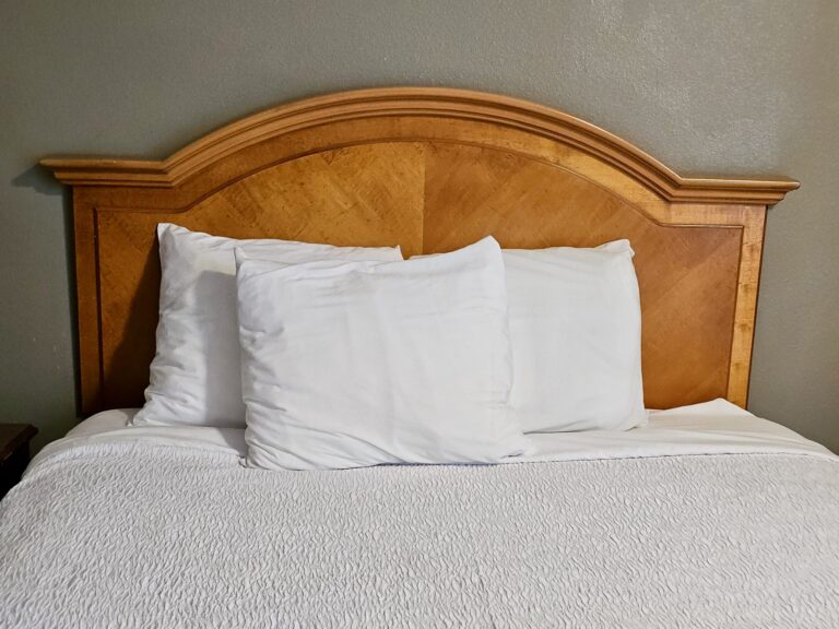 Neatly made bed with white pillows and white bedding against a wooden headboard