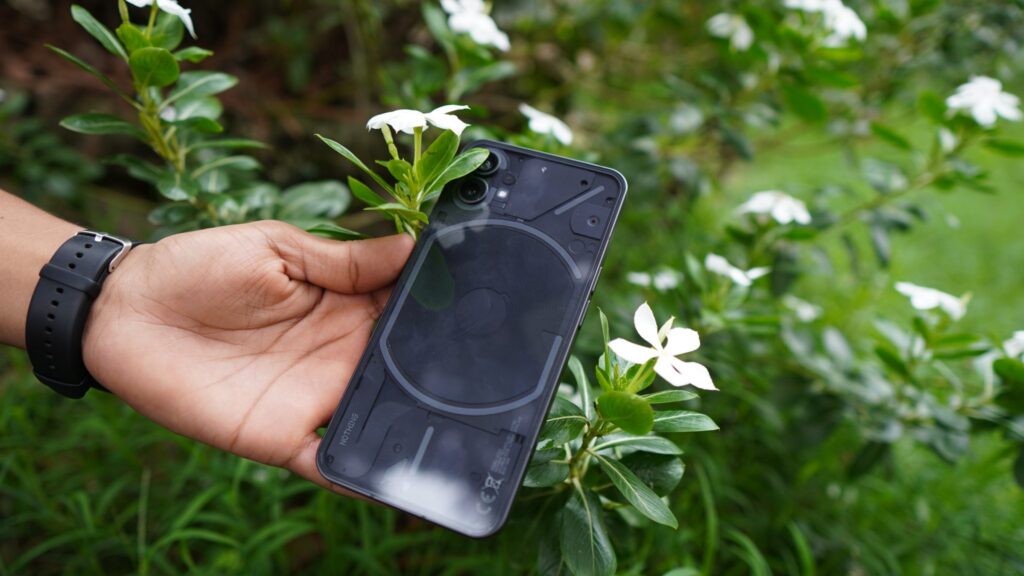 Hand holding a smartphone in front of white flowers and green leaves