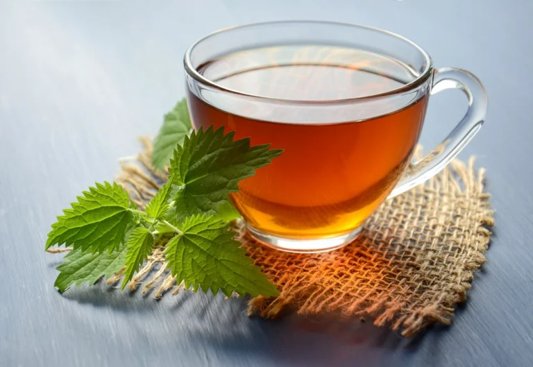 Glass cup of warm herbal tea on a woven mat beside fresh green mint leaves
