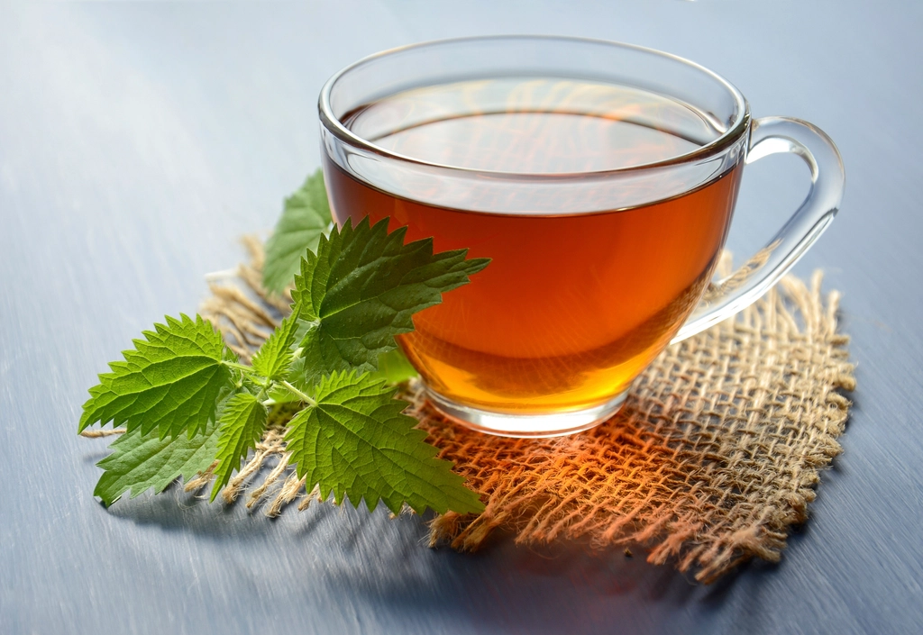 Glass cup of warm herbal tea on a woven mat beside fresh green mint leaves
