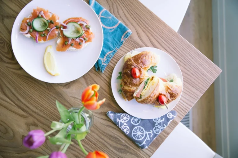 Brunch plates with sandwiches and salmon toast beside colorful tulips on a wooden table