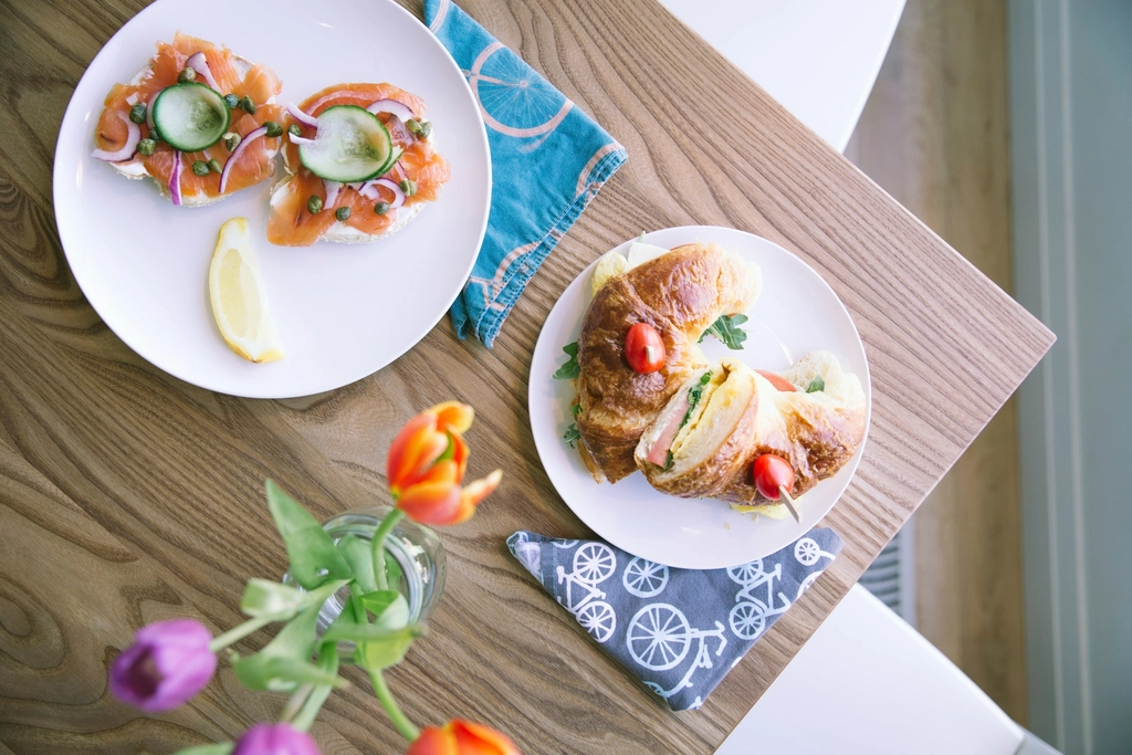 Brunch plates with sandwiches and salmon toast beside colorful tulips on a wooden table