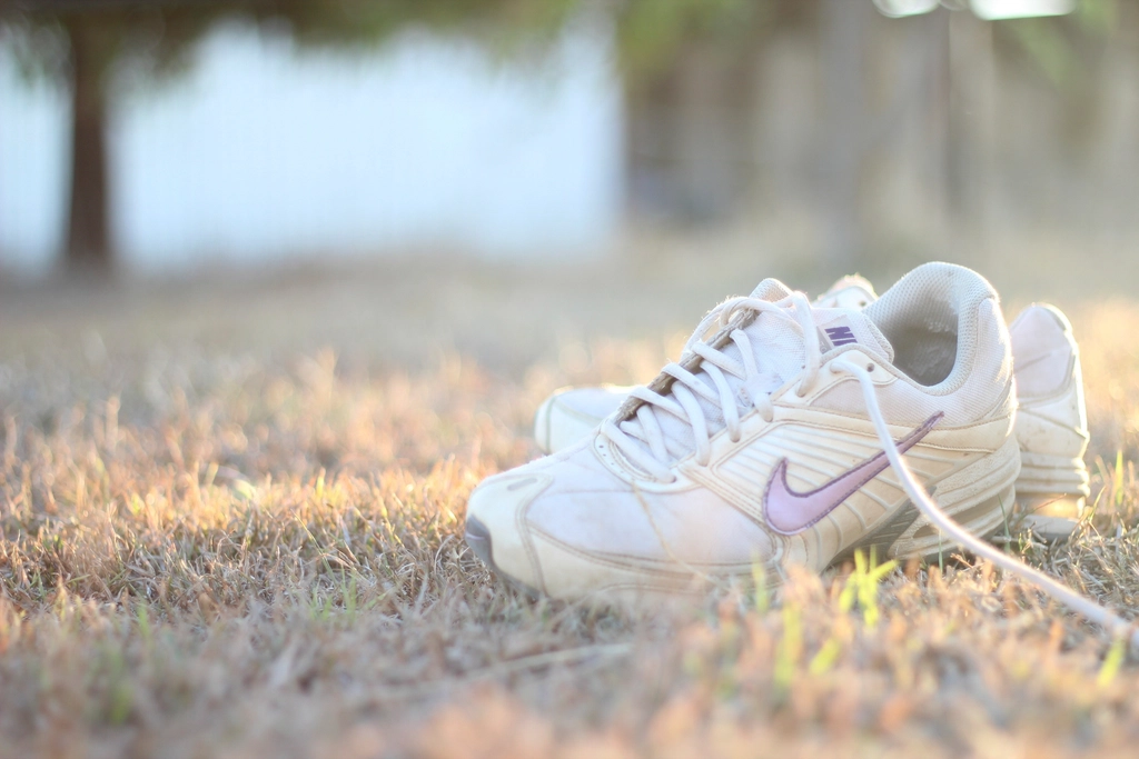 Pair of white running shoes resting on sunny grass