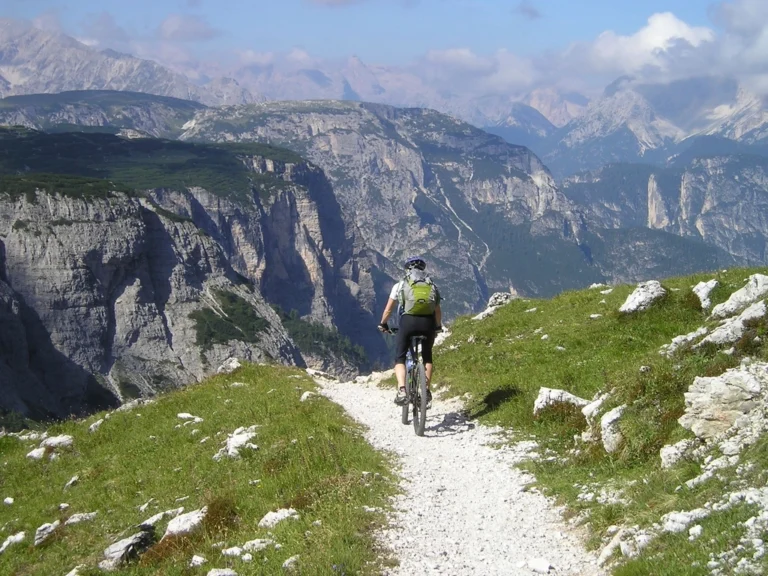 Man riding a mountain bike along a sunny trail through green alpine hills