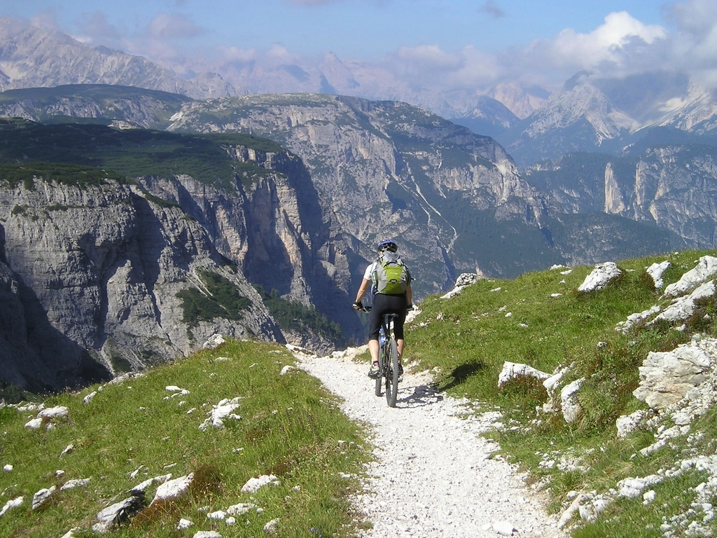 Man riding a mountain bike along a sunny trail through green alpine hills