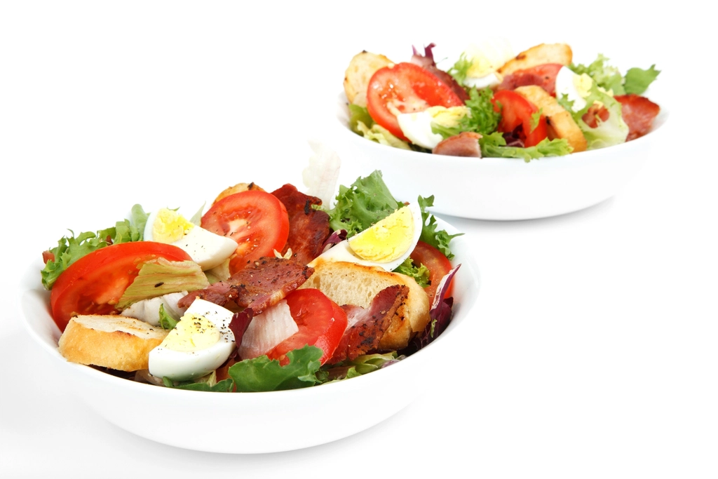 Two white bowls of fresh salad with tomatoes, eggs and greens