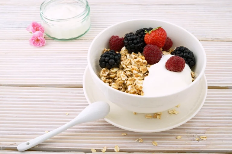 Bowl of yogurt topped with granola and fresh berries on a white wooden table