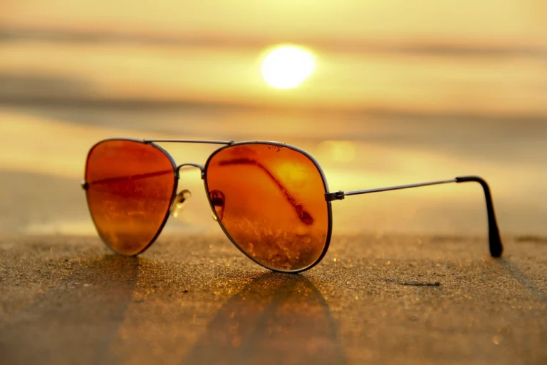 Orange aviator sunglasses resting on sand at a golden beach sunset