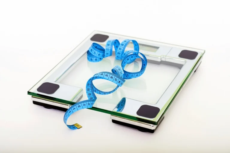 Glass bathroom scale with a blue measuring tape on a white background