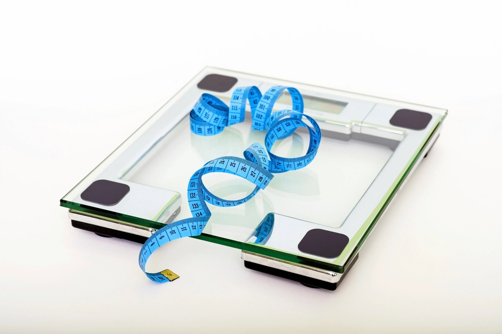 Glass bathroom scale with a blue measuring tape on a white background