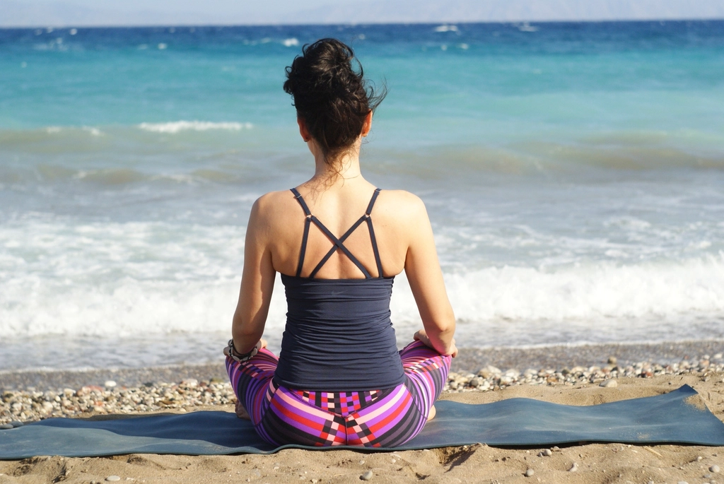 Woman sitting cross-legged on a yoga mat on the beach facing the sea