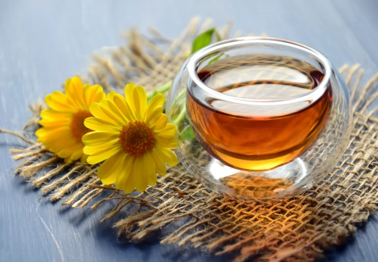 Glass cup of warm herbal tea beside yellow daisies on a woven mat