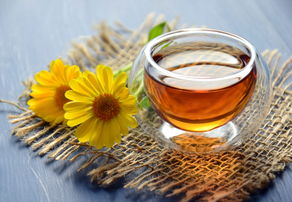 Glass cup of warm herbal tea beside yellow daisies on a woven mat