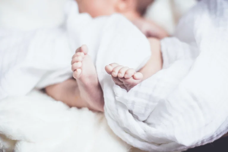 Tiny baby feet peeking out from a soft white blanket